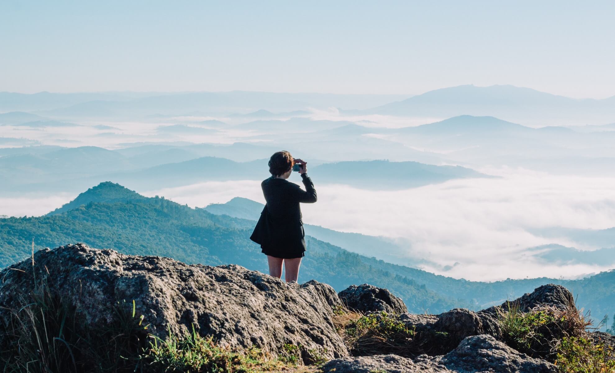 jeune femme surplombant des montagnes en train de prendre des photos